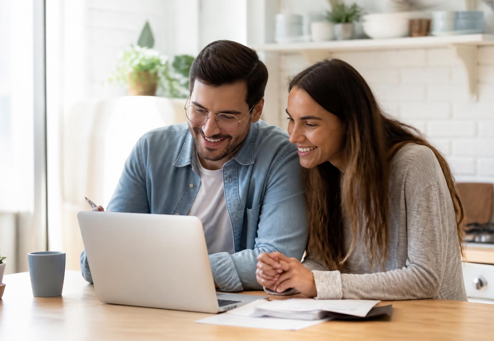 A couple reviewing their savings on a laptop at a bright kitchen table